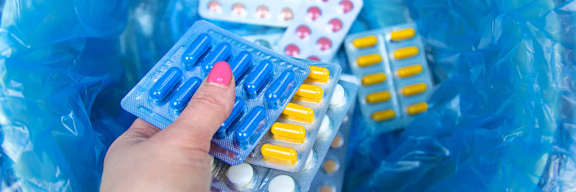 Eine Frauenhand wirft mehrere Tabletten in einen Mülleimer.