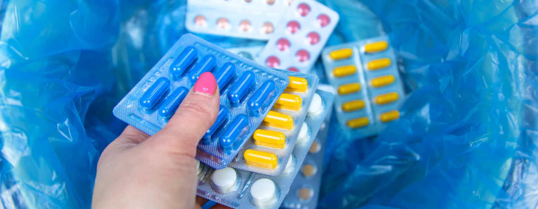 Eine Frauenhand wirft mehrere Tabletten in einen Mülleimer.