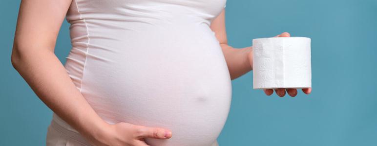 Hämorrhoiden in der Schwangerschaft: Hochschwangere Frau hält eine Rolle Klopapier neben ihrem Bauch.