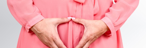 Frau im Kleid hält Hände vor das Becken.