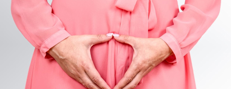 Frau im Kleid hält Hände vor das Becken.