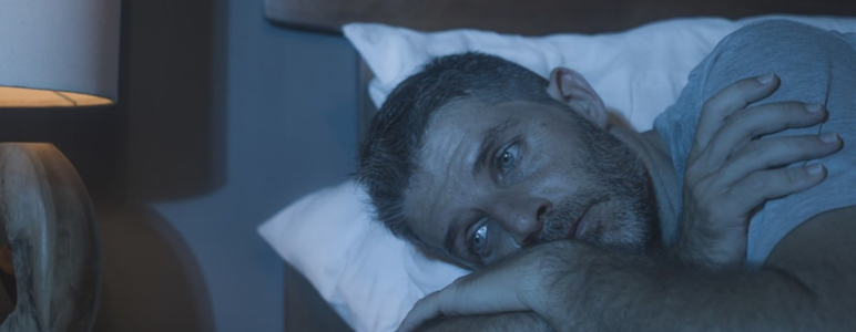 Ein Mann liegt in einem abgedunkelten Raum schlaflos im Bett.