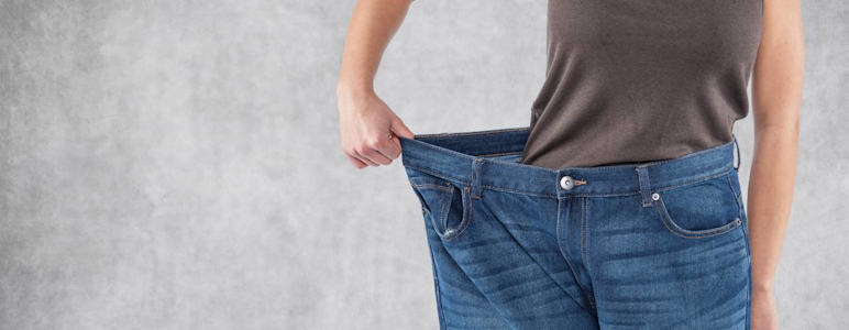 Frau hält zu große Jeanshose mit einer Hand an der Hüfte.