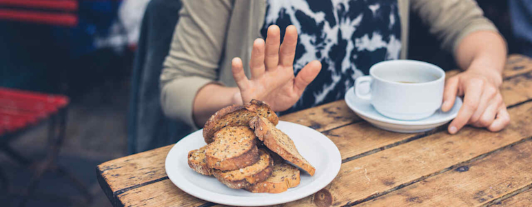Eine Frau trinkt Kaffee und lehnt das angebotene Brot ab.