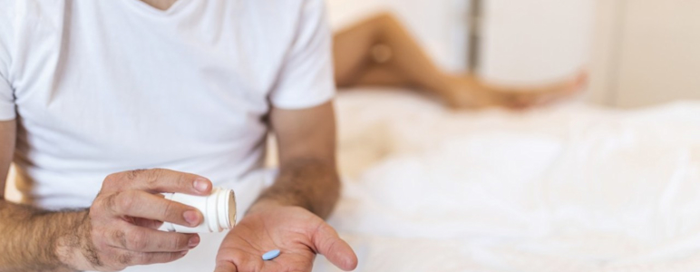 Mann sitzt auf Bett mit Viagra Pille auf der Hand.