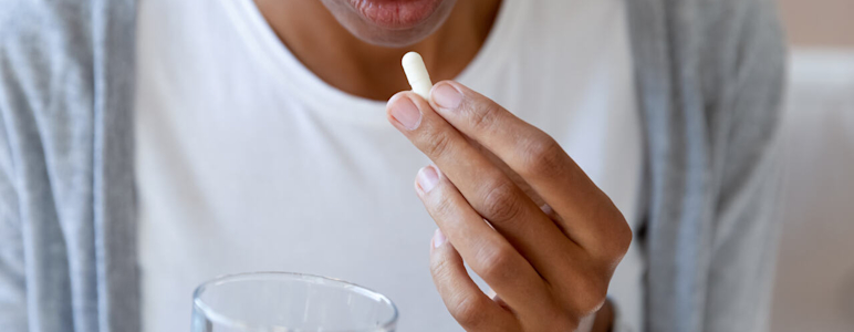 Eine Frau nimmt Antibiotika als Kapseln mit einem Glas Wasser ein.