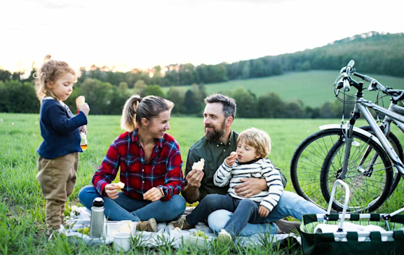 Familie mit zwei Kindern sitzt beim Picknick im Grünen.