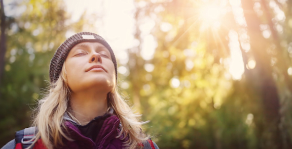 Frau mit Mütze atmet frische Luft im Wald bei Sonnenschein.