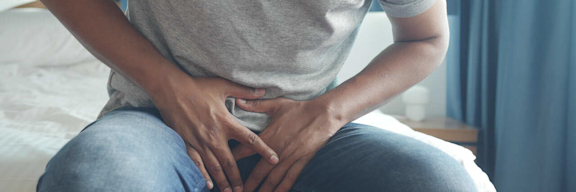 Ein junger Mann hält sich vor Schmerzen die Hände in den Schoß.