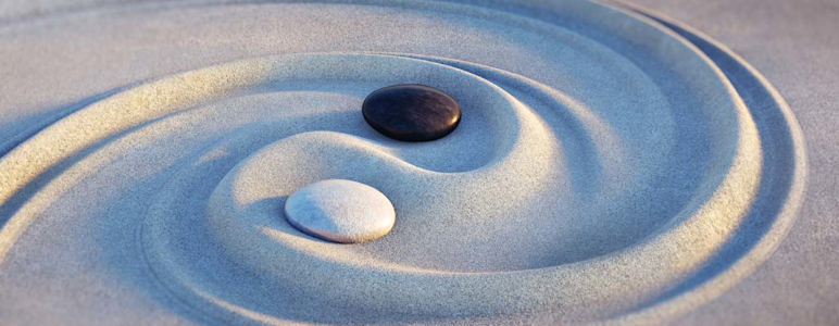 Ying und Yang wurde in den Sand gezeichnet. Die Symbolik wird durch einen schwarzen und einen weißen Stein verdeutlicht.