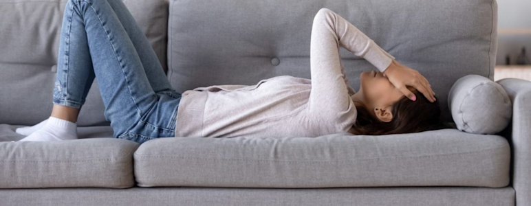 Eine Frau hat vestibuläre Migräne und liegt mit Kopfschmerzen und Schwindel auf dem Sofa.