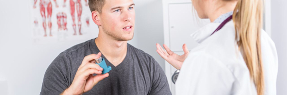 Ein Patient hält ein Asthmaspray in der Hand und redet mit einer Ärztin.