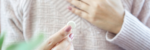 Frau hält mit der einen Hand die schmerzende Brust und in der anderen Hand eine Tablette.