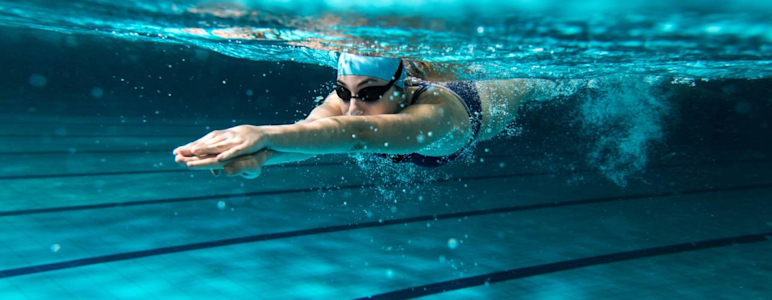 Junge Frau schwimmt im Schwimmbad und taucht gerade ins Wasser ein.
