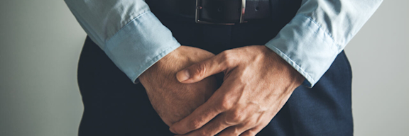 Mann mit Anzug hält sich den Schritt.