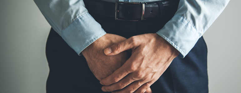 Mann mit Anzug hält sich den Schritt.