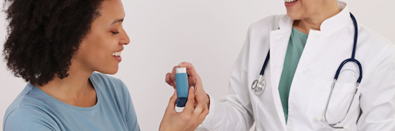 Eine Ärztin reicht einer Patientin mit Asthma einen Inhalator.