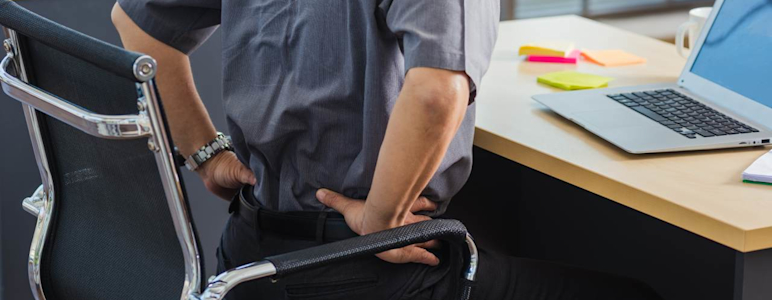Ein Mann sitzt am Schreibtisch auf einem Bürostuhl und hält sich den Rücken.