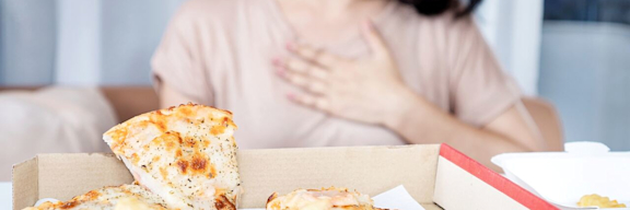 Frau hält sich die Hand an das Brustbein, nachdem sie Pizza und Pommes gegessen hat.