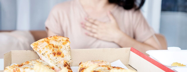 Frau hält sich die Hand an das Brustbein, nachdem sie Pizza und Pommes gegessen hat.