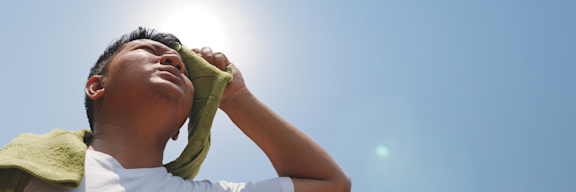 Mann trocknet schwitzendes Gesicht mit grünem Handtuch in der prallen Sonne