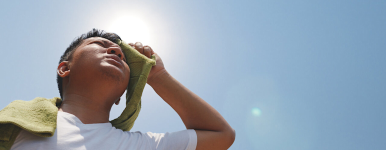 Mann trocknet schwitzendes Gesicht mit grünem Handtuch in der prallen Sonne