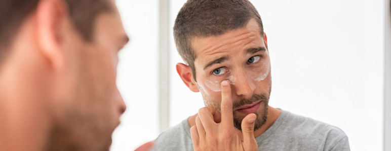 Junger Mann trägt ein Pflegeprodukt auf die Hautpartie unter den Augen auf.