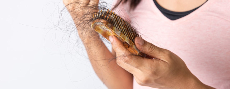 Es ist der Oberkörper und die Hände einer Frau zu sehen. Sie hält eine Bürste in der Hand in der sich ein Haarbüschel befindet.