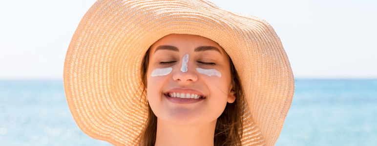 Junge Frau am Meer, die einen Sonnenhut trägt und Sonnencreme im Gesicht hat.
