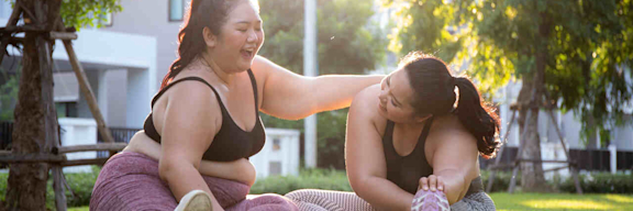 Zwei Übergewichtige Frauen machen Yoga-Übungen im Park und haben Spaß dabei.