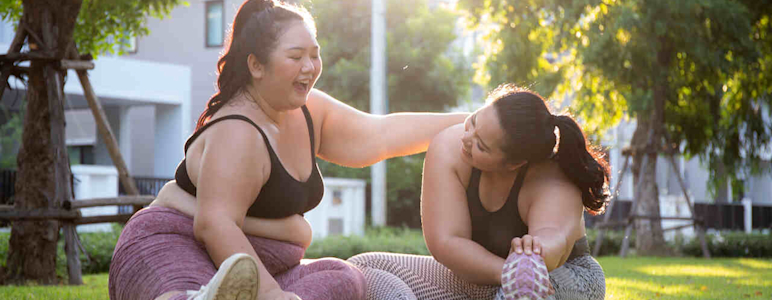 Zwei Übergewichtige Frauen machen Yoga-Übungen im Park und haben Spaß dabei.