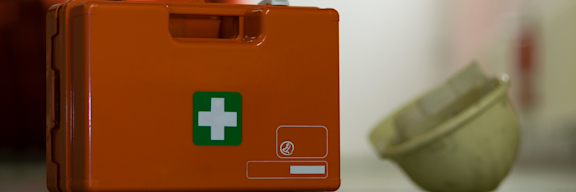 Neben einem Erste-Hilfe-Koffer liegt ein Schutzhelm.