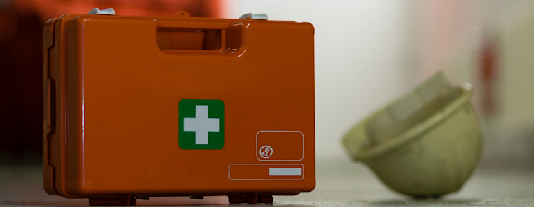 Neben einem Erste-Hilfe-Koffer liegt ein Schutzhelm.