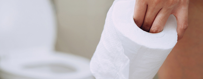 Eine Frauenhand hält eine Rolle Klopapier, im Hintergrund ist eine Toilette zu sehen.