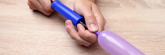 Ein länglicher Luftballon wird mit einer Luftpumpe befüllt.