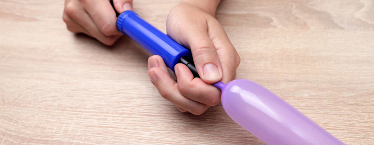 Ein länglicher Luftballon wird mit einer Luftpumpe befüllt.