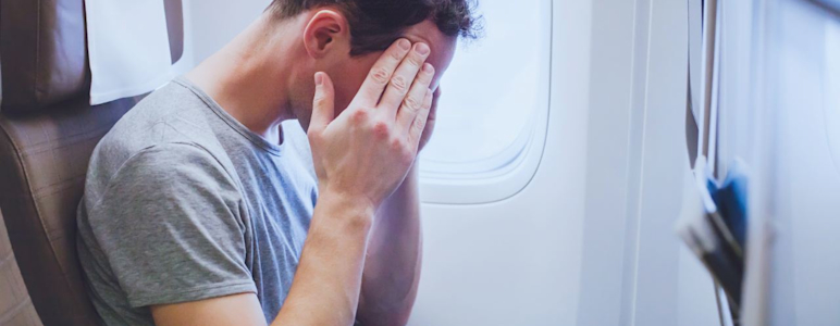 Mann sitzt im Flugzeug und hält sich die Hände vor das Gesicht.