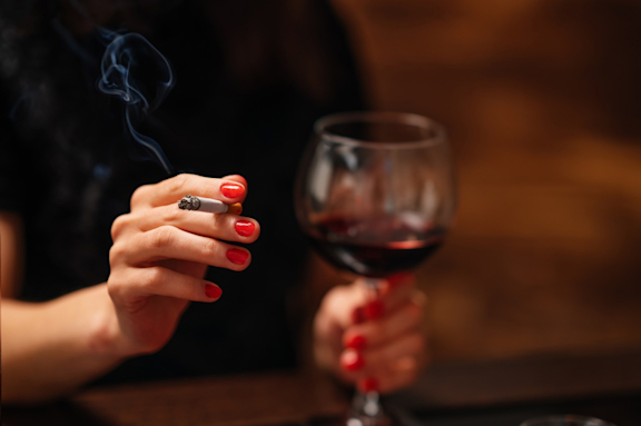 Eine Frau hält eine Zigarette und ein Glas mit Rotwein in der Hand.