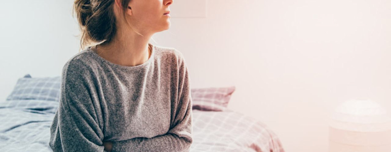 Eine Frau sitzt auf dem Bett und hält sich vor Schmerzen den Bauch.