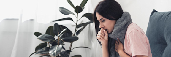 Kranke Frau sitzt im Bett und hustet.