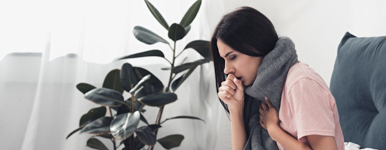 Kranke Frau sitzt im Bett und hustet.