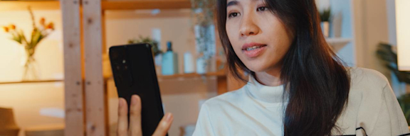 Junge Frau hält Smartphone in der Hand und führt ein Videotelefonat.
