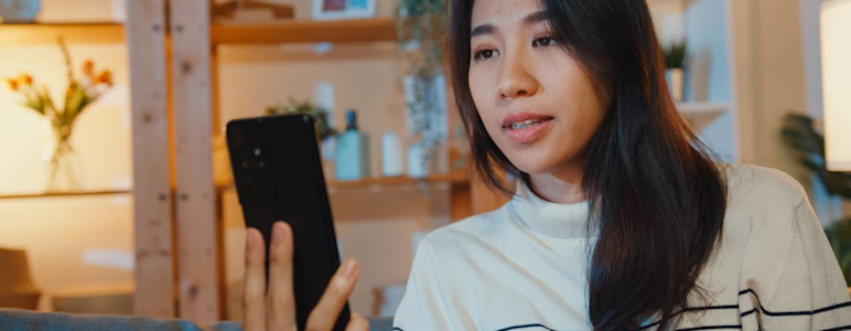 Junge Frau hält Smartphone in der Hand und führt ein Videotelefonat.