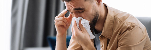 Mann mit Nasennebenhöhlenentzündung (Sinusitis) und Schnupfen schnäuzt sich in ein Taschentuch.