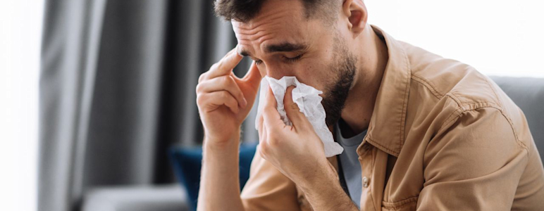 Mann mit Nasennebenhöhlenentzündung (Sinusitis) und Schnupfen schnäuzt sich in ein Taschentuch.