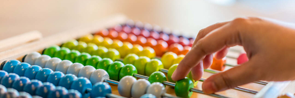 Eine Hand schiebt bunte Perlen zur Berechnung mithilfe eines Abakus hin und her.