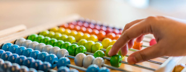 Eine Hand schiebt bunte Perlen zur Berechnung mithilfe eines Abakus hin und her.
