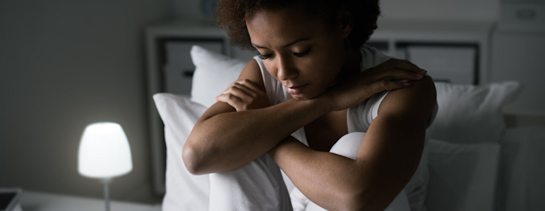 Eine junge Frau sitzt niedergeschlagen auf einem Bett.