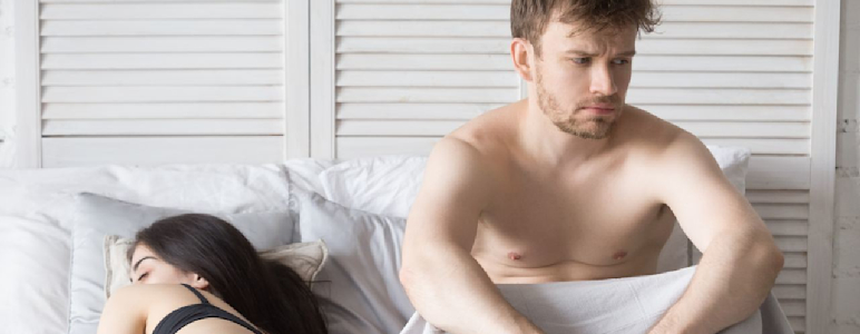 Mann und Frau im Bett. Die Frau schläft, der Mann ist wach und frustriert.