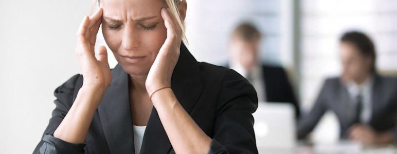 Eine Frau sitzt im Büro und hält sich die Schläfen während eines schmerzhaften Migräneanfalls.